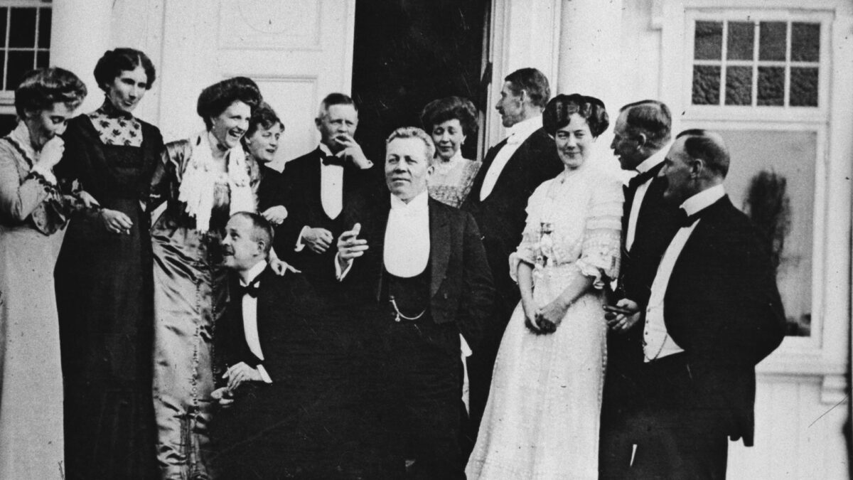Historien om Losby Gods. Festkledde og feststemte mennesker på trappen utenfor gamlegodset